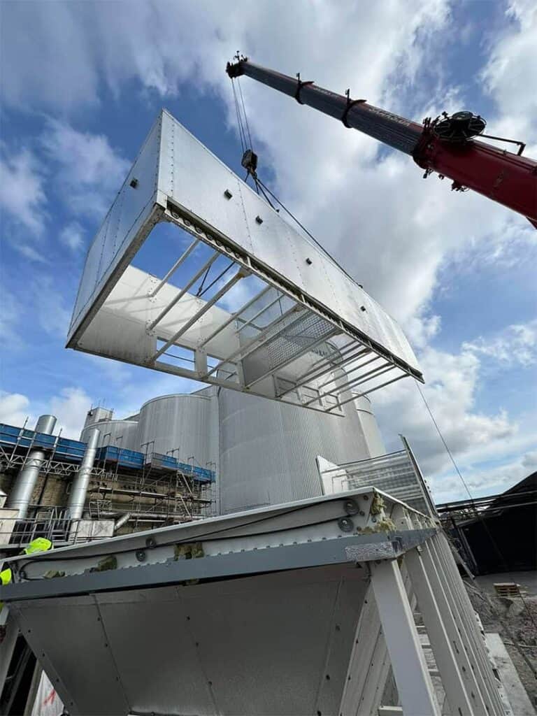 Kran løfter en stor ventilationskanal op på en industribygning