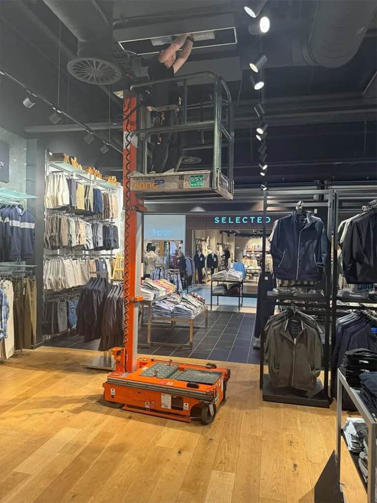 Montør monterer ventilation i loftet i en tøjbutik fra sakselift