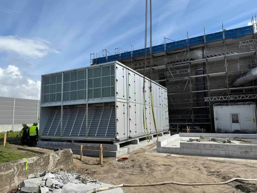 Stort ventilationsaggregat opstillet på fundament ved en byggeplads