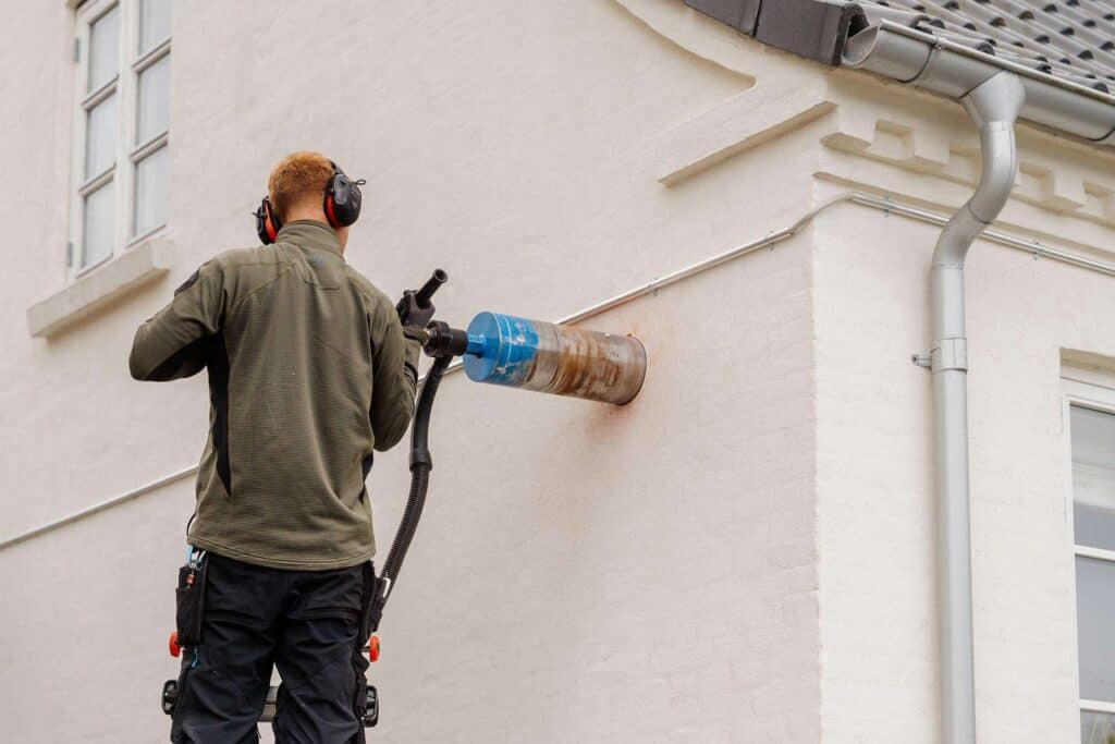 Montør borer hul til enrumsventilation i en husfacade
