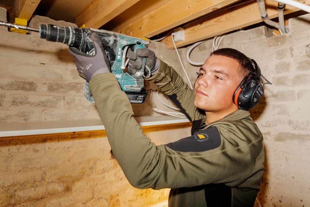 Montør borer gennem ydervæggen fra loftet ved montering af ventilation