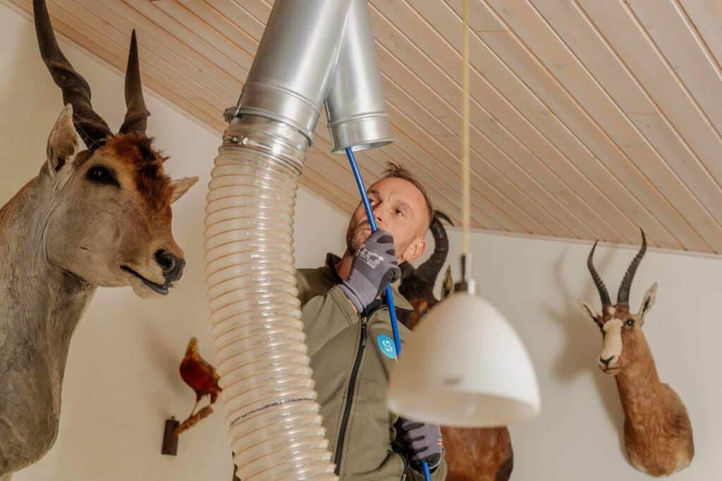 Montør renser en ventilationskanal i loftet med børste